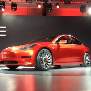 Ein roter Tesla Model drei steht auf einer Bühne und wird beleuchtet.